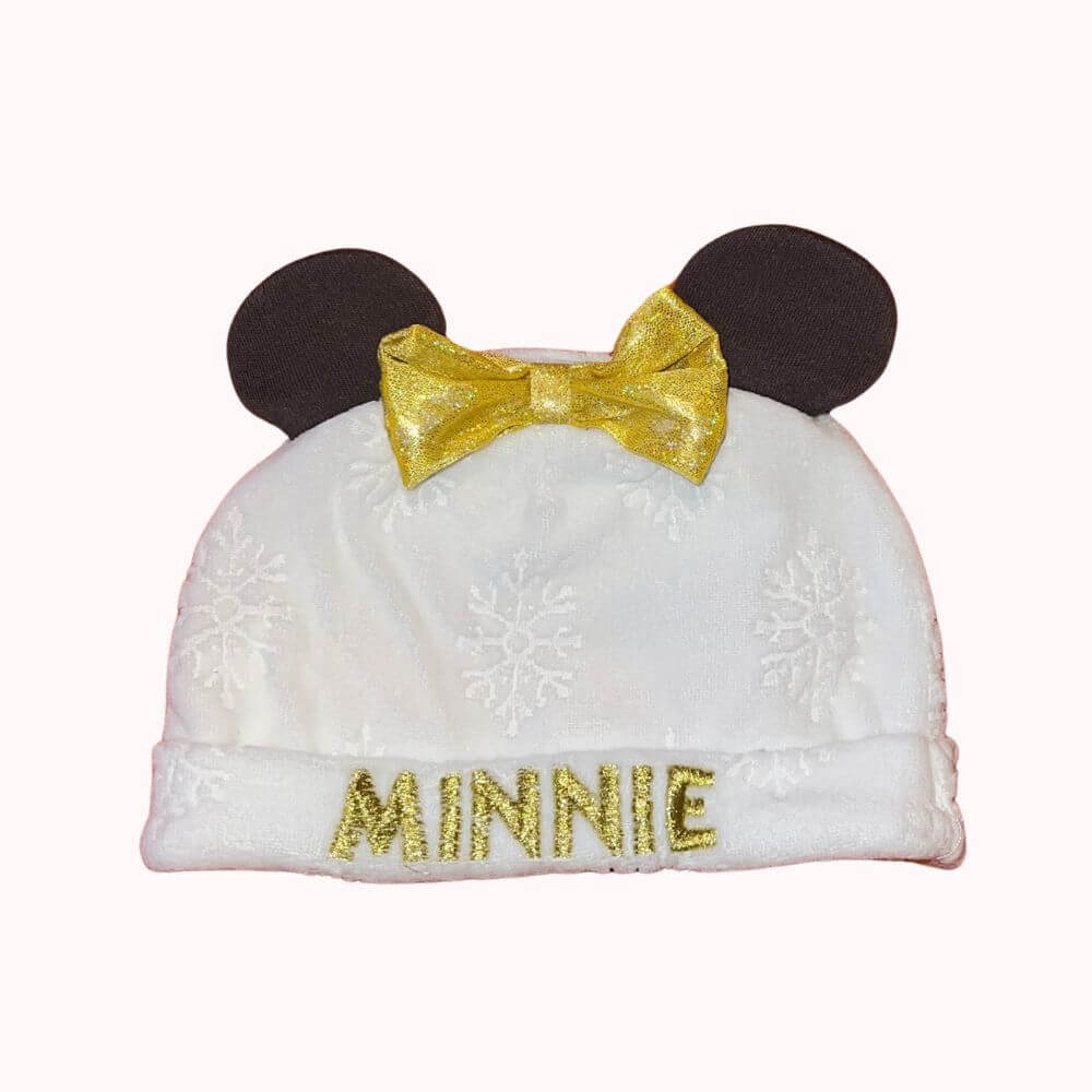 Bonnet bébé blanc à motif flocons avec oreilles noires, nœud doré brillant et inscription « Minnie » brodée en fil doré.