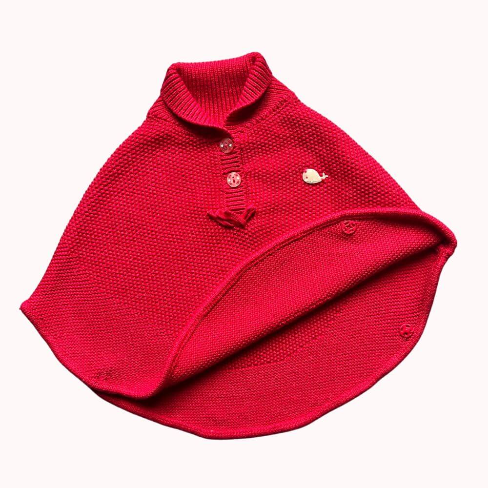 Cape en maille rouge pour bébé 6 mois avec boutons à l’encolure et broche baleine décorative.
