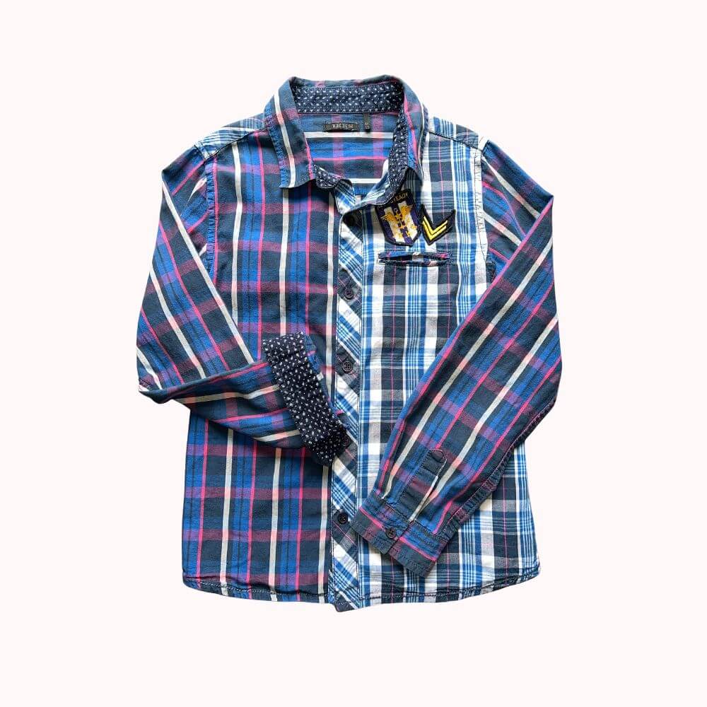 Chemise classique à carreaux bleu rose blanc , asymétrique au niveau des couleurs. Coté gauche dominance bleu ciel et coté droit dominance bleu foncé, intérieur des poignets et du col doublé tissu noir à motif géométriques blancs. Poche poitrine côté gauche , avec écussons de la marque.