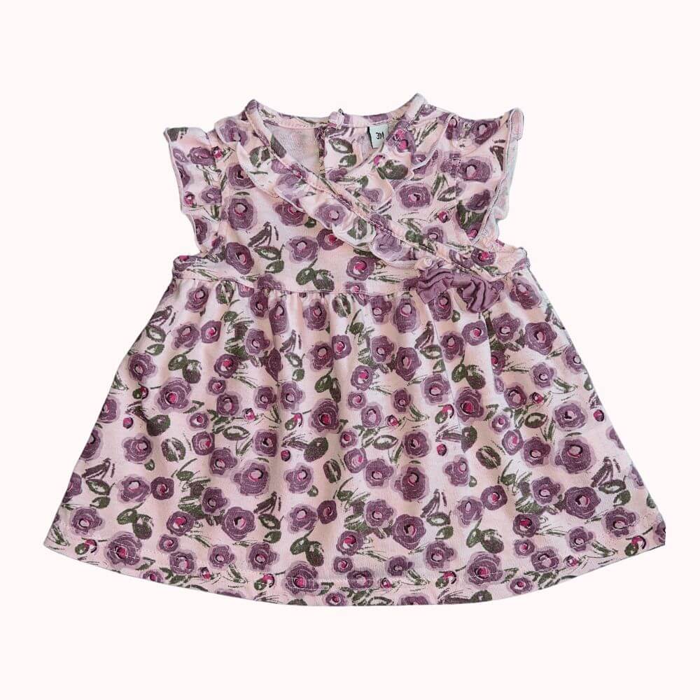 Robe fleurie pour enfant avec imprimé violet, encolure volantée croisée, fleur décorative sur le côté, et boutons dans le dos, en très bon état.