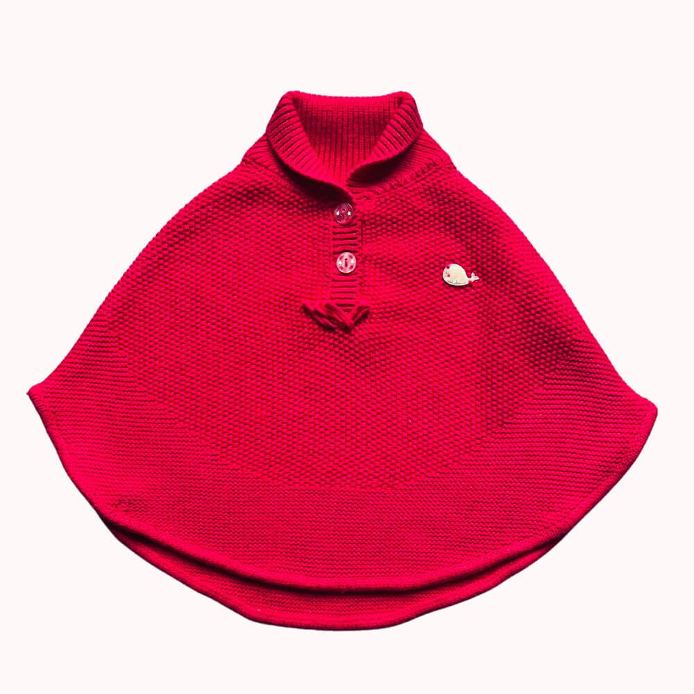Cape en maille rouge pour bébé 6 mois avec boutons à l’encolure et broche baleine décorative.
