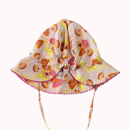 Chapeau de soleil DPAM, 18-24 mois, imprimé fleuri coloré avec liens à nouer et large visière bordée de petits pompons roses.