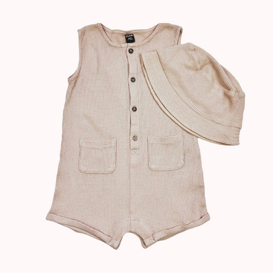 Combinaison écru en coton gaufré sans manches avec boutons en bois et poches plaquées, accompagnée d’un chapeau assorti.
