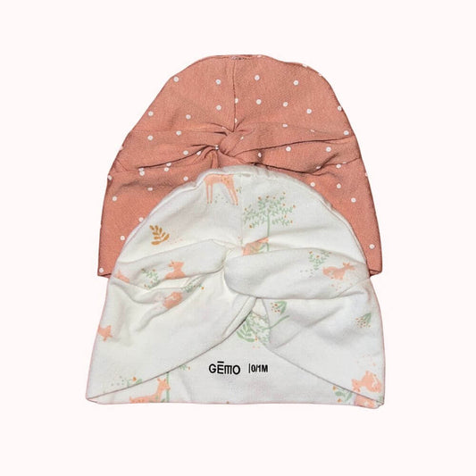 Lot de deux bonnets naissance Gémo, un rose à pois blancs et un blanc à motifs de faons et feuillages, avec nœud sur le devant.