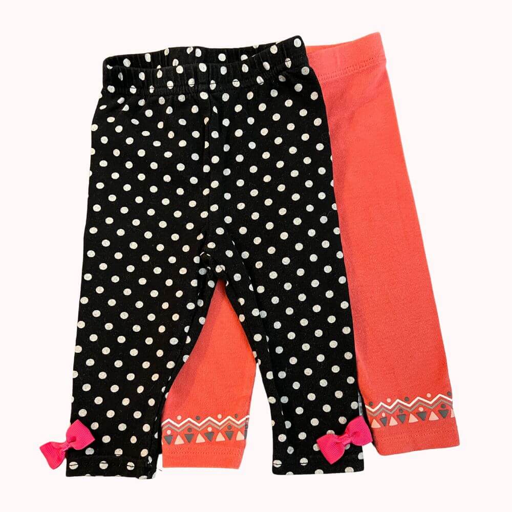Lot de deux leggings bébé taille 6 mois : un noir à pois blancs avec nœuds roses, un corail avec motif géométrique au bas des jambes.