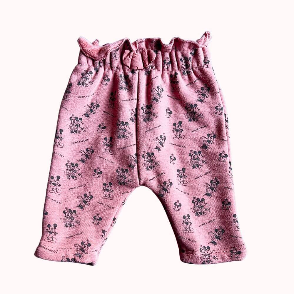 Pantalon rose bébé à taille élastiquée avec nœud décoratif, imprimé Mickey et Minnie en noir, en bon état.