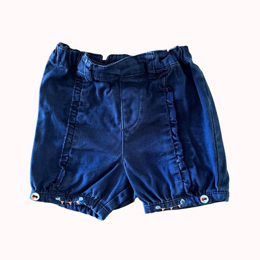 Short bleu marine pour bébé fille, avec volants latéraux, taille élastiquée et boutons fantaisie aux chevilles.