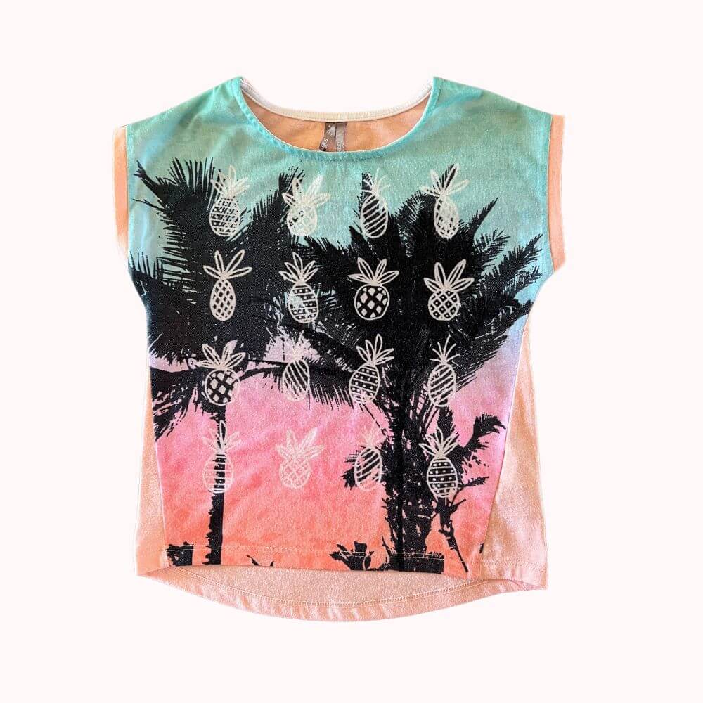 T-shirt à manches courtes pour enfant, imprimé palmiers et ananas sur fond dégradé pastel, coupe fluide et légère.