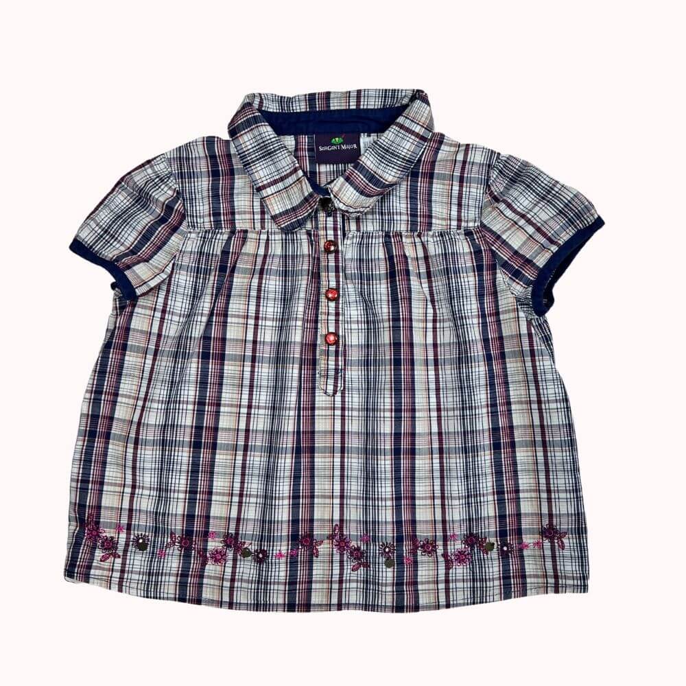 Tunique à carreaux pour enfant, manches courtes, col arrondi, broderies fleuries en bas et fermeture boutonnée.
